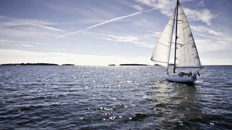 Classic yacht sailing away against blue sky